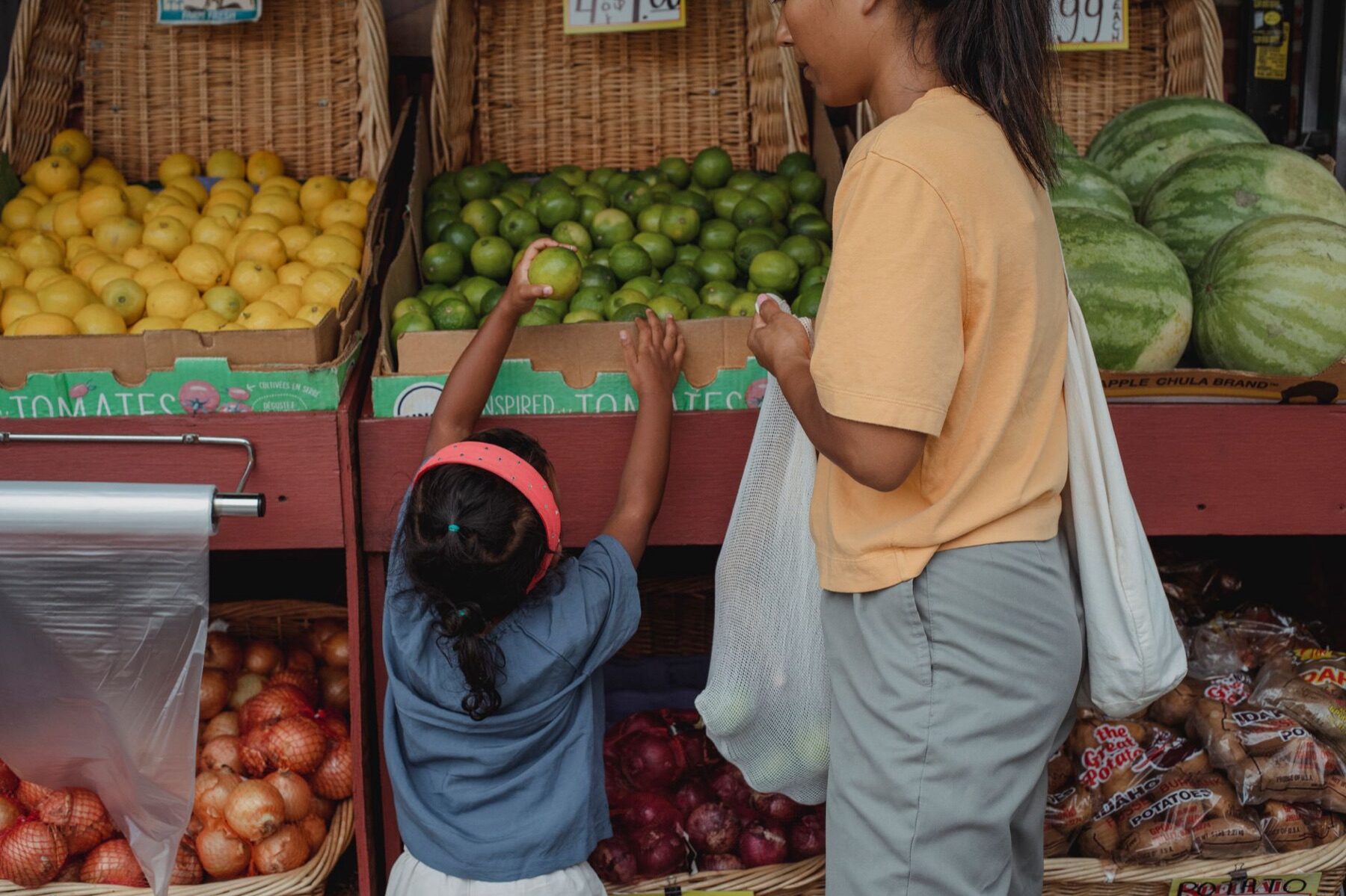 Mother and young daughter choosing fresh fruit from crates of lemons and limes at an outdoor produce market