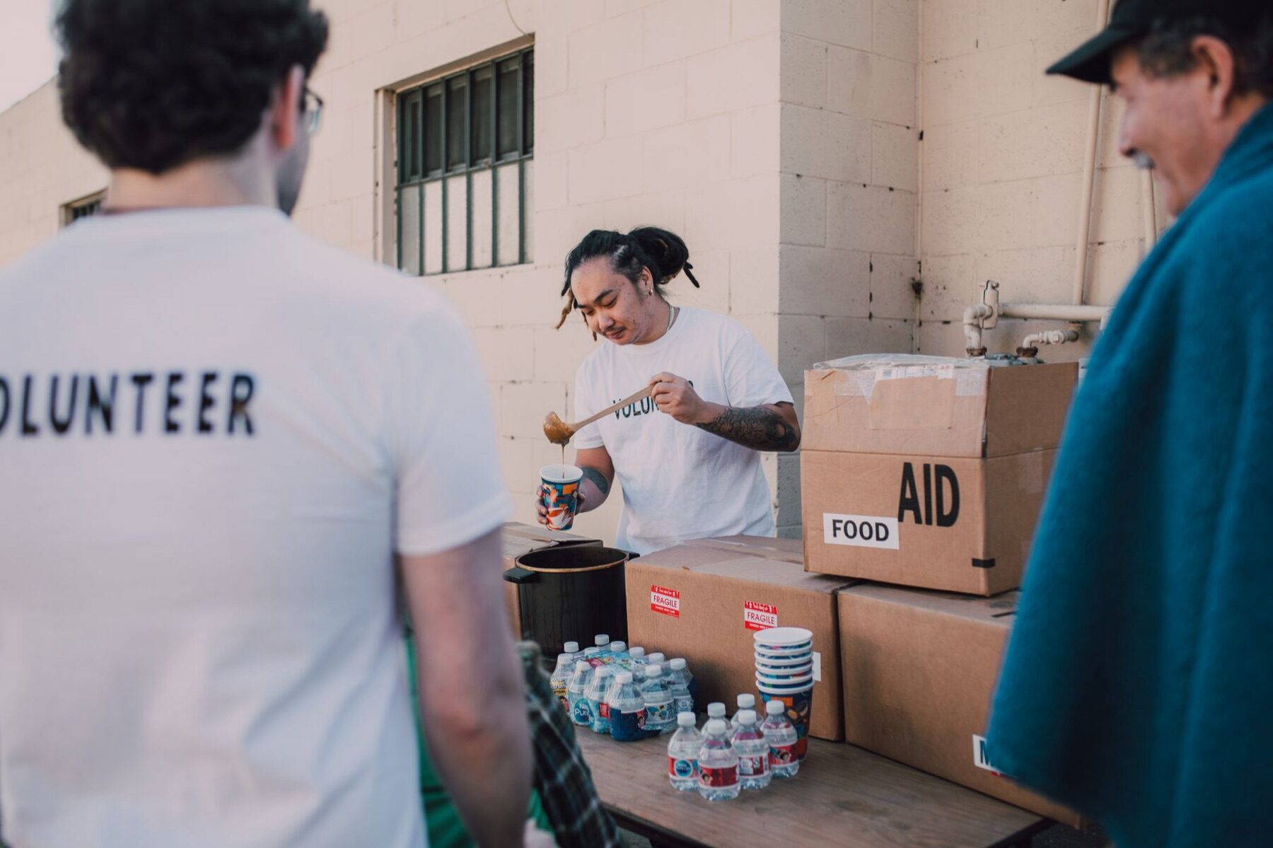 Volunteer serving food at an outdoor distribution table between two community members